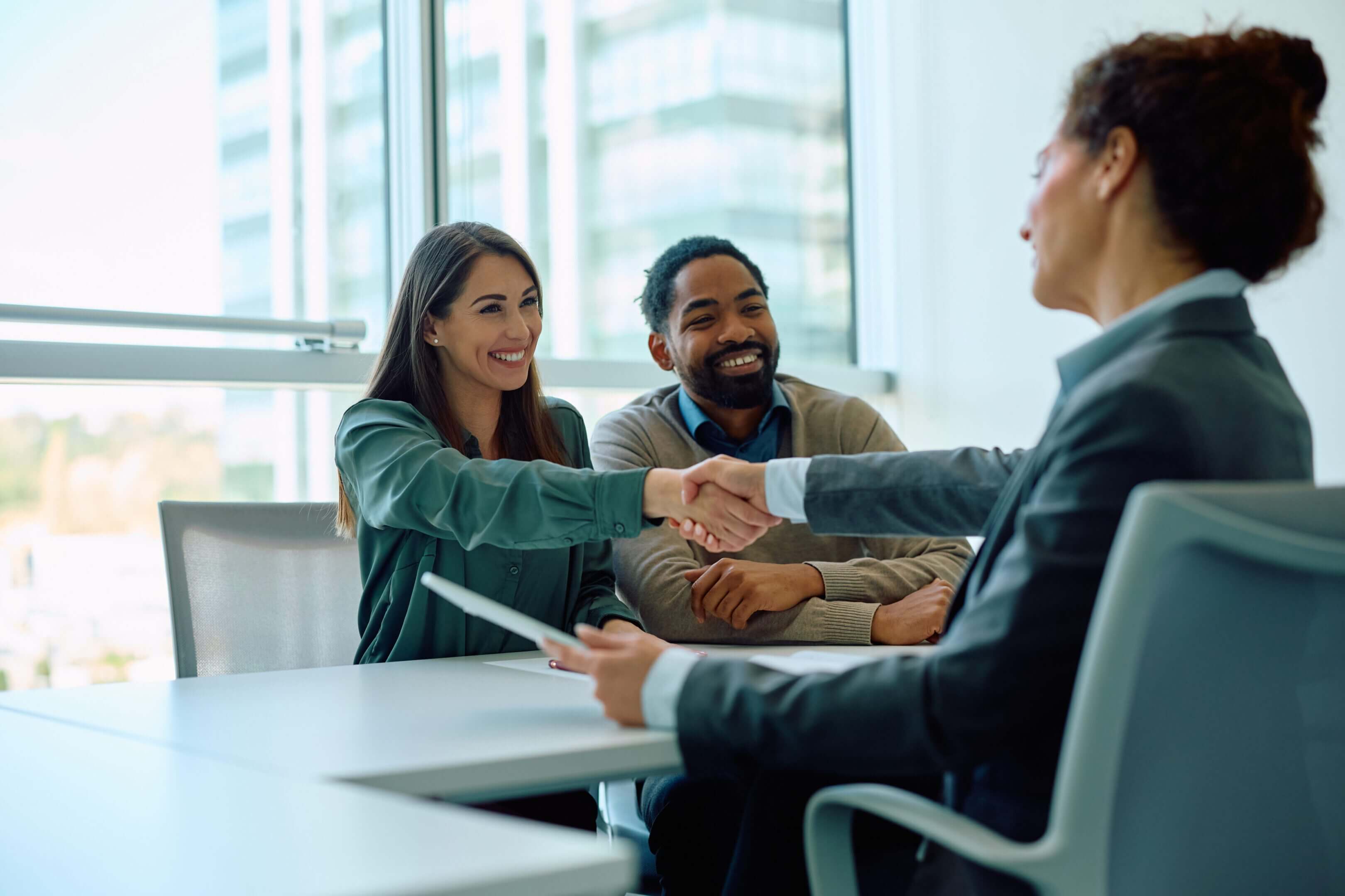 Two professionals shaking hands with a third person at a meeting.