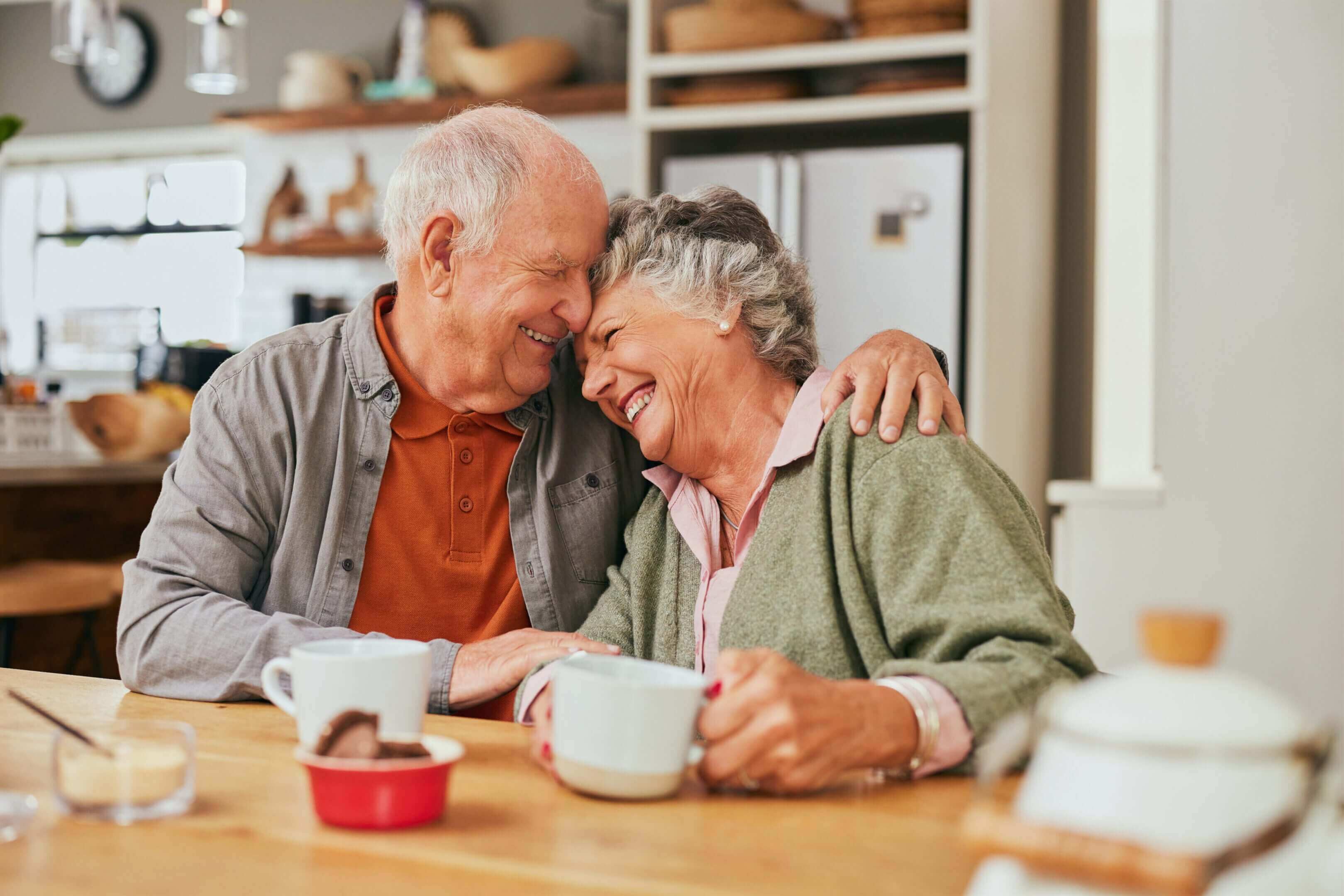 Elderly couple laughing over coffee at home.